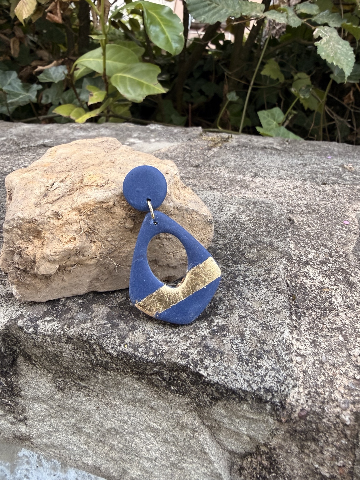 Blue handmade earring with a gold accent resting against a stone