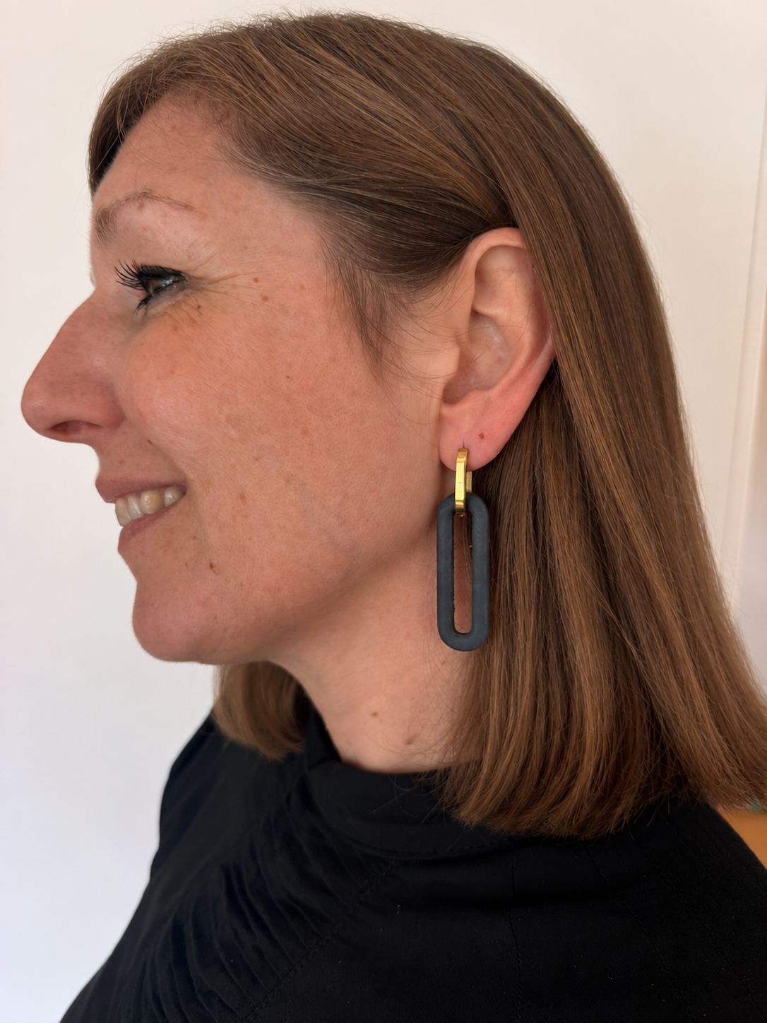 Woman with naturally styled hair wearing a dark rectangular Monopops earring
