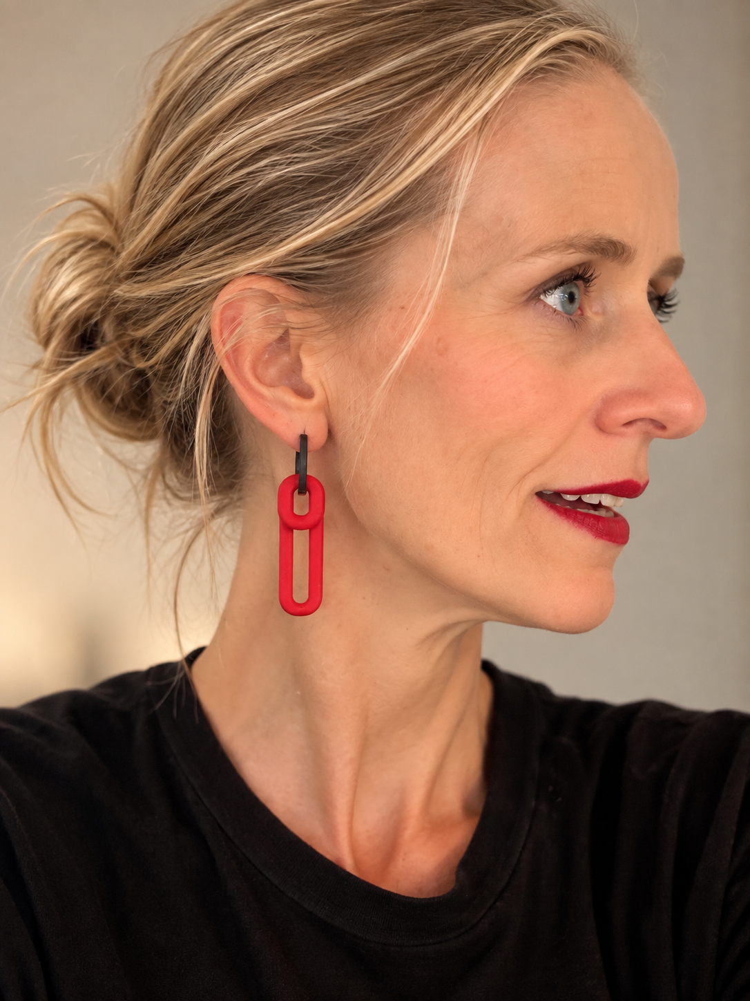 Woman in side profile wearing a red double-loop Monopops earring and a black top